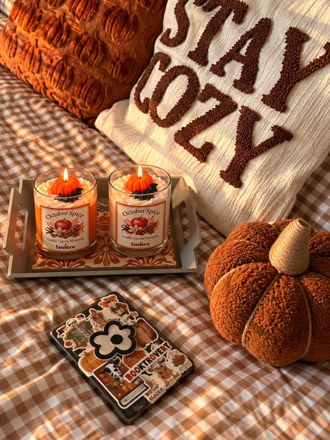 Dos velas October Spice sobre una bandeja junto a cojines y calabazas de tejido
